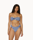 A woman wearing a blue and white striped bikini standing in front of a white wall.