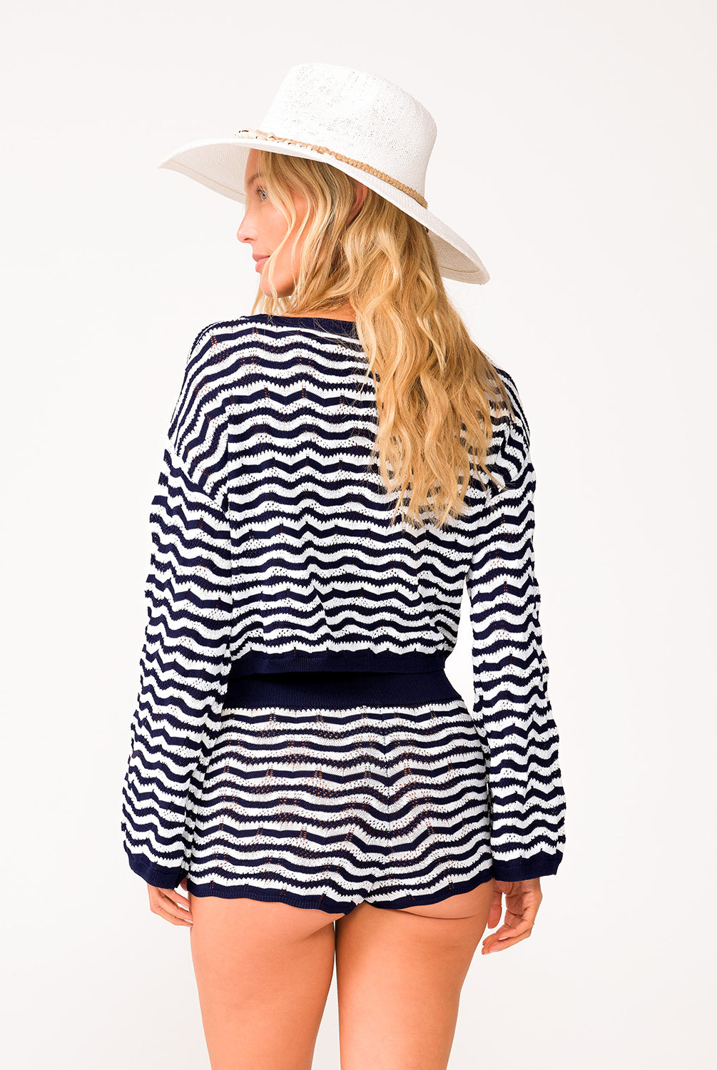A woman wearing a long sleeve blue and white striped top and matching shorts facing towards a white wall.