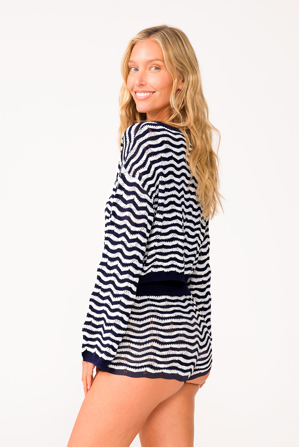 A woman wearing a long sleeve blue and white striped top and matching shorts standing in front of a white wall.