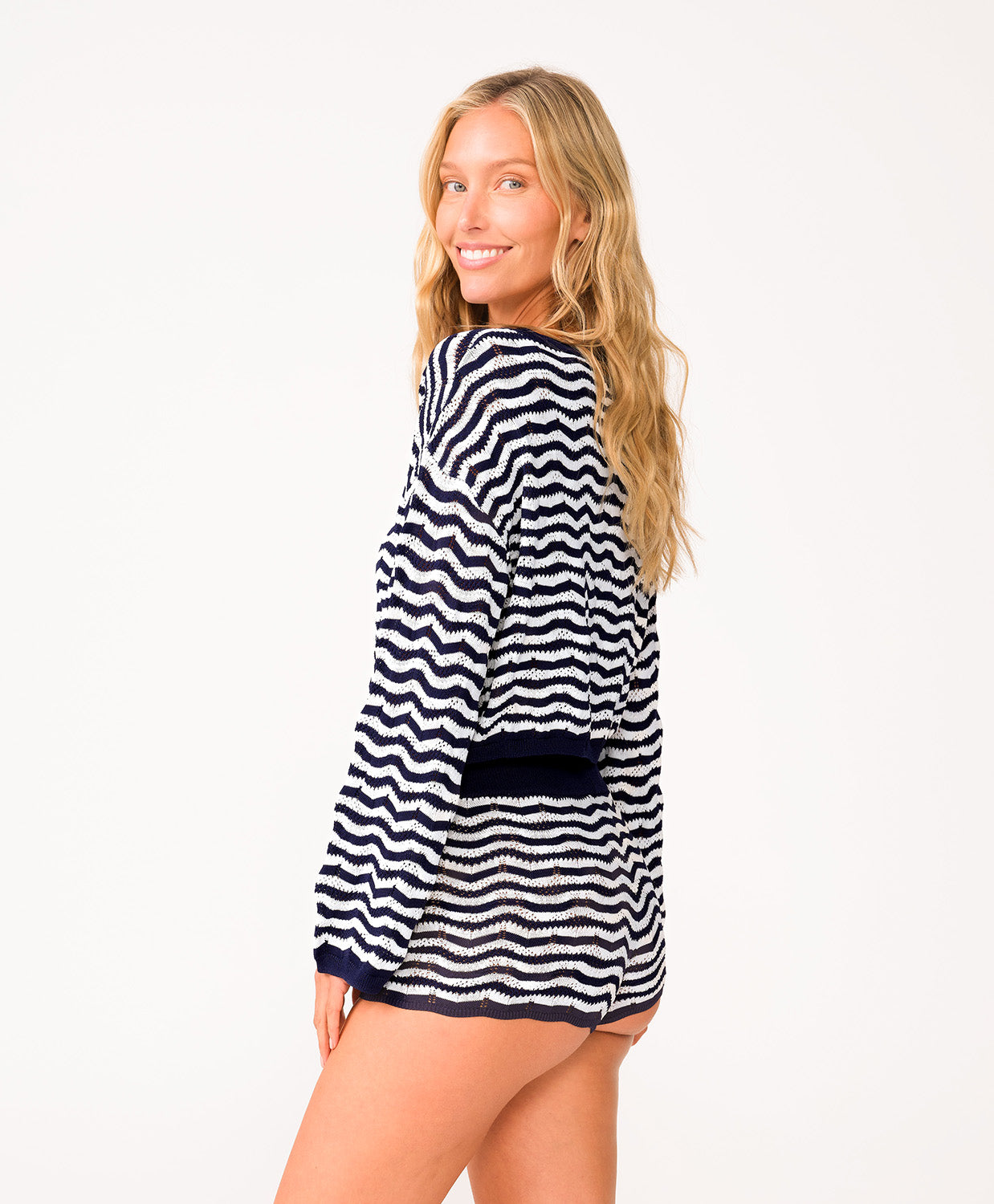 A woman wearing a long sleeve blue and white striped top and matching shorts standing in front of a white wall.