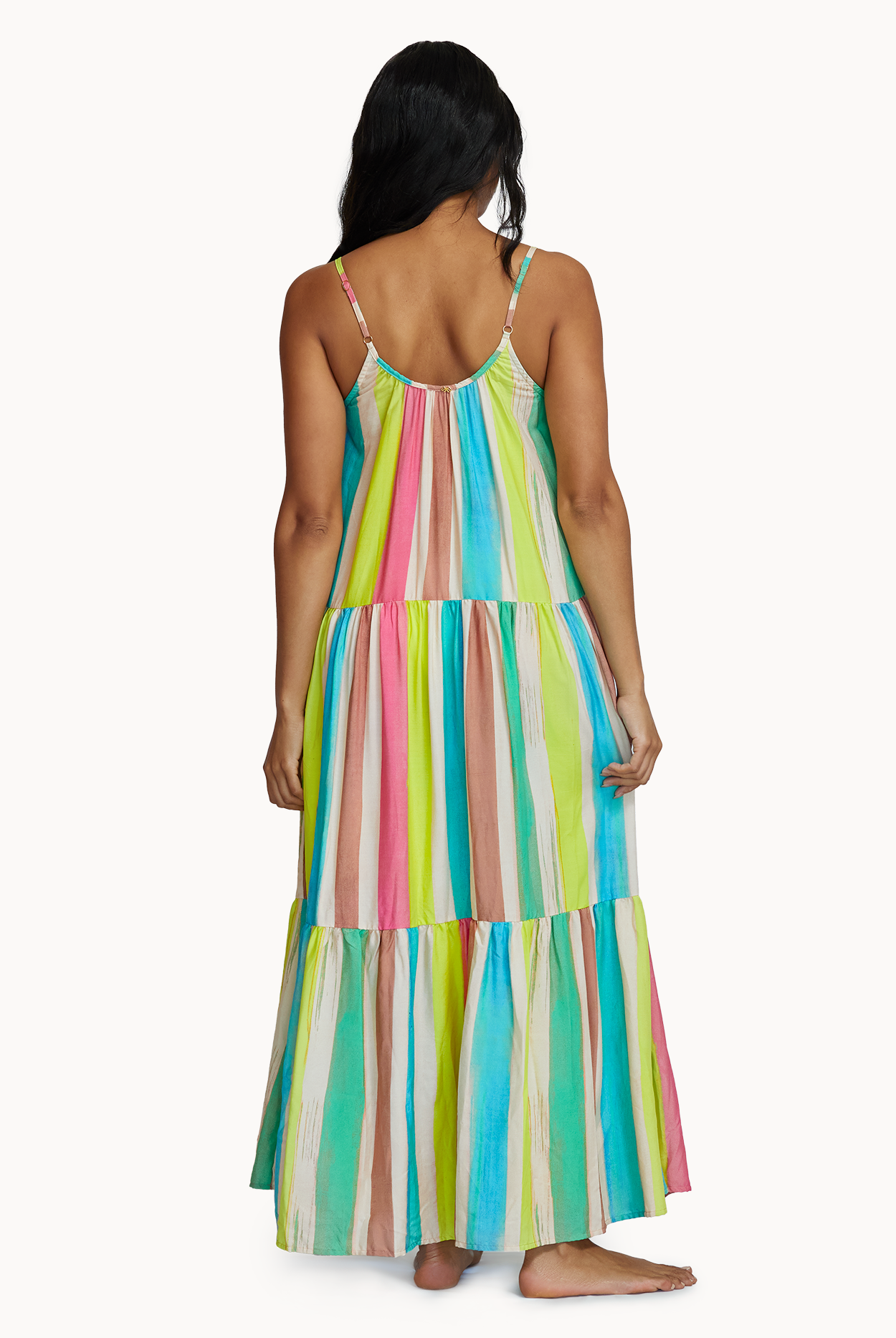 A woman wearing a floor length multi colored dress facing towards a white wall.