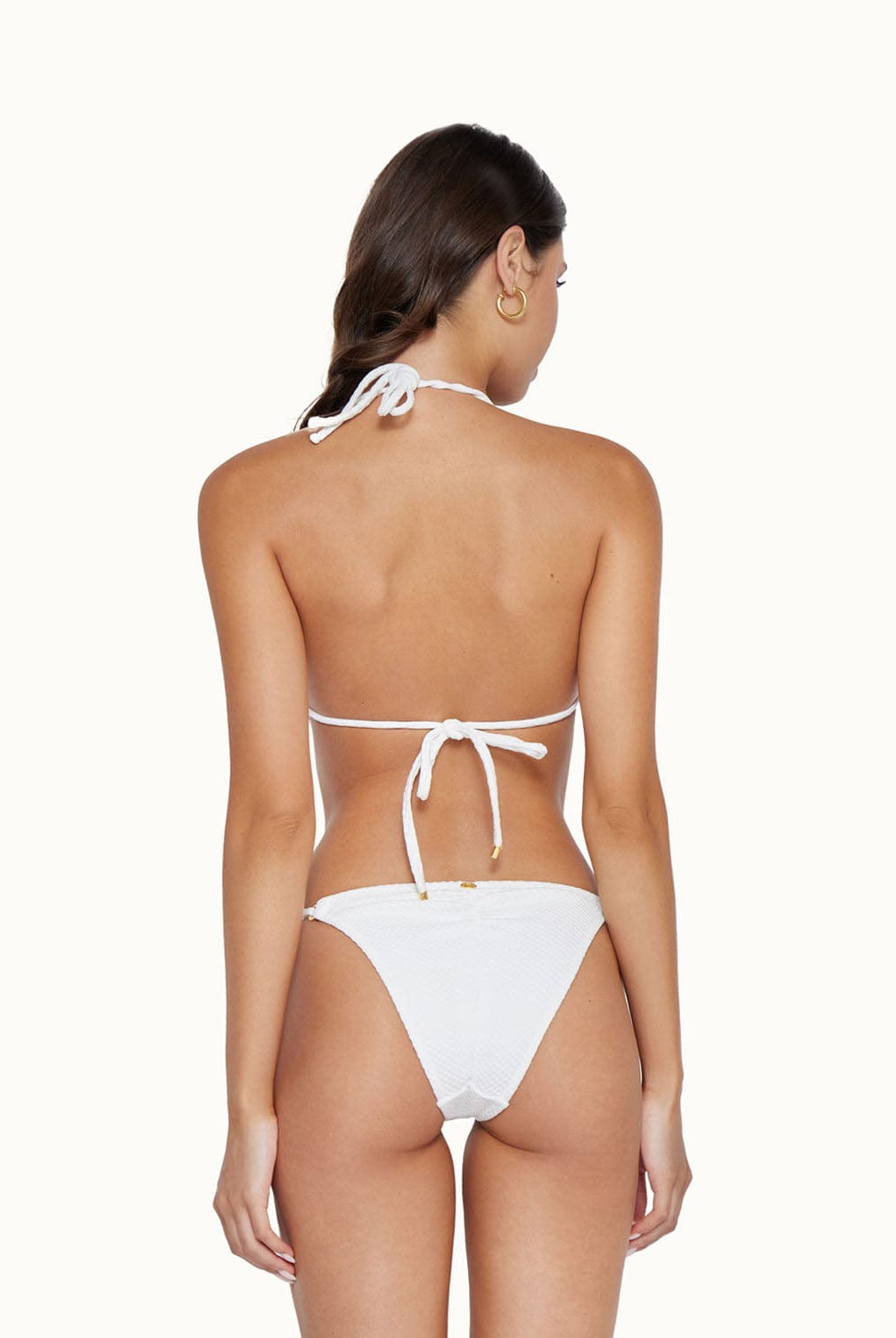 Back view of brunette woman wearing a white bikini in front of a white background.
