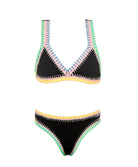 A black bikini with colorful embroidery against a white wall.