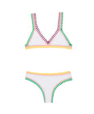 A white kids bikini with colorful embroidered trim against a white wall.