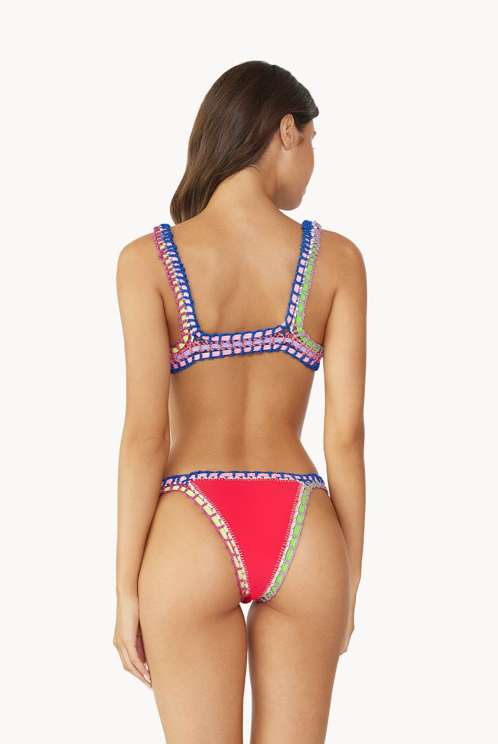 A brunette woman wearing a red bikini facing towards a white wall.