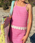 Young girl wearing a pink crochet dress with a colorful bag on a sandy background