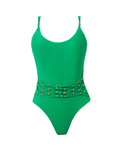 A green one piece swimsuit with gold beading. Featured against a white wall background.
