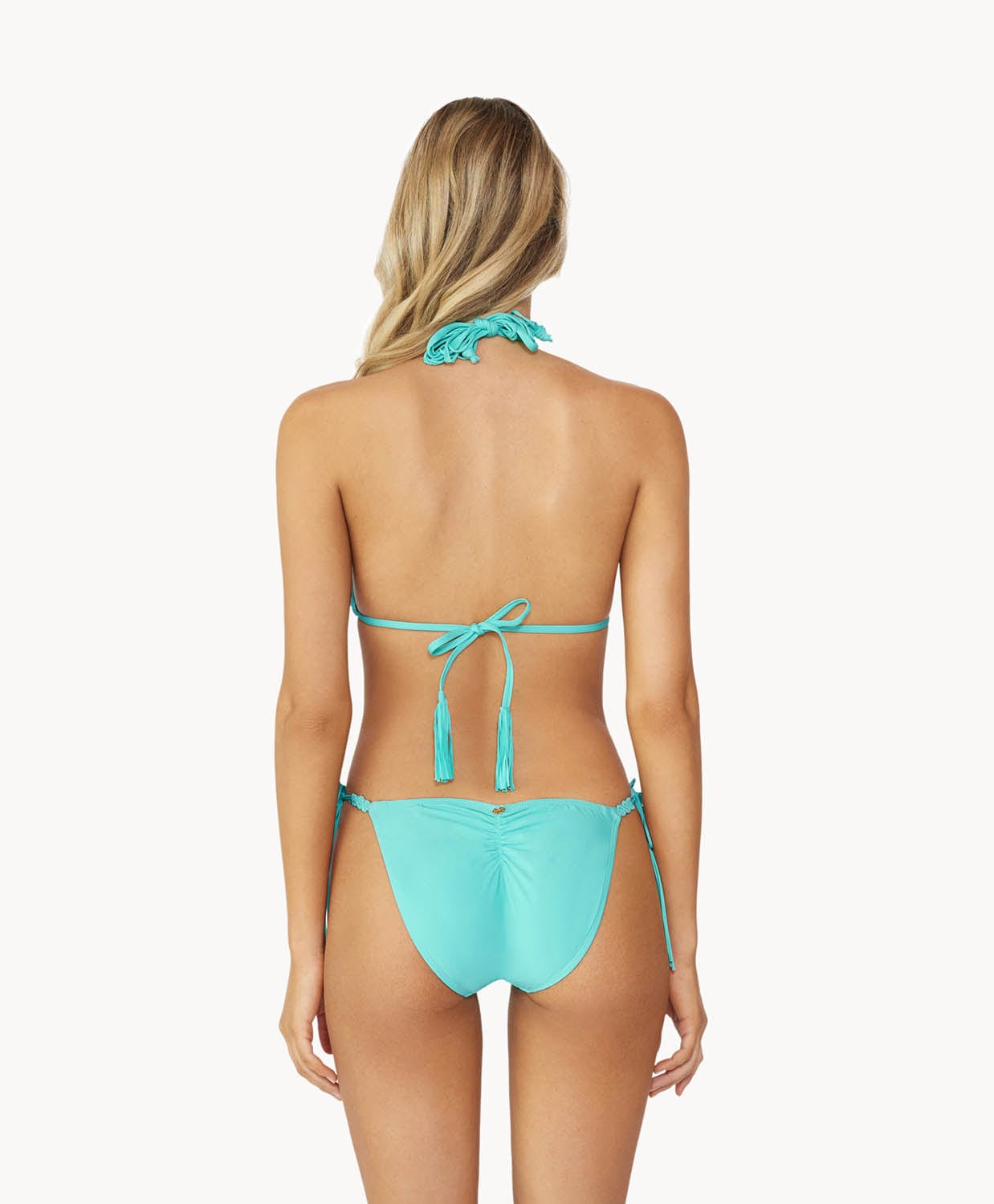 A blonde woman wearing a turquoise bikini facing towards a white wall.