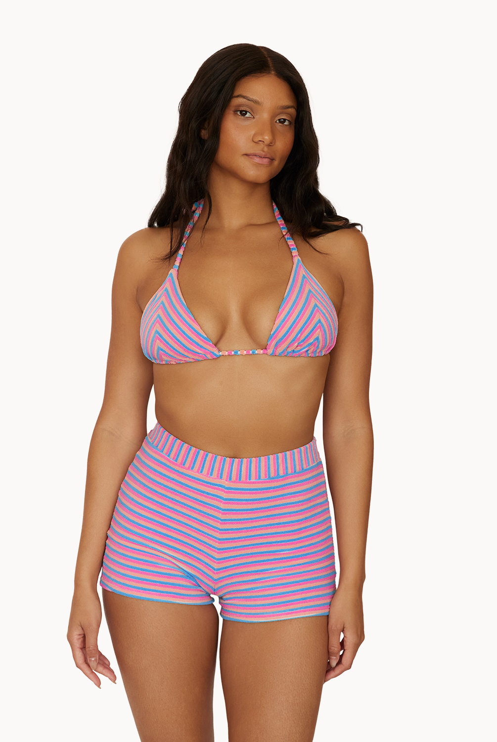 A woman wearing a striped bikini top and shorts standing in front of a white wall.