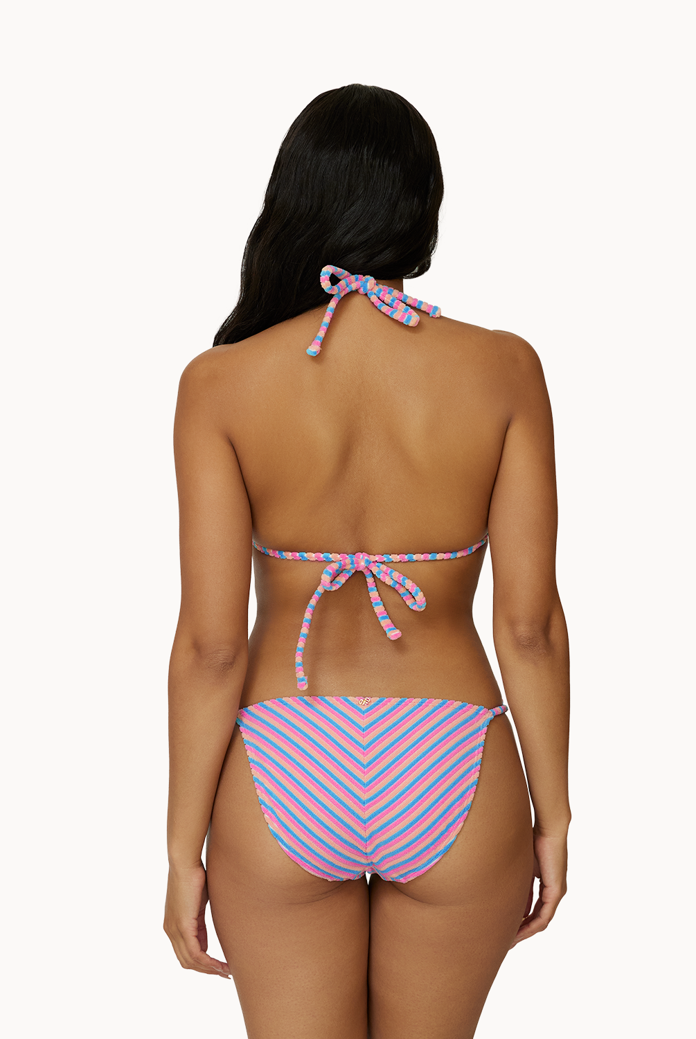 A woman wearing a striped bikini facing towards a white wall.