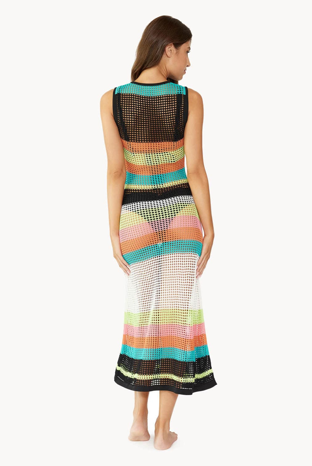 Brunette woman wearing a multi-colored striped full length dress facing backwards towards white wall.