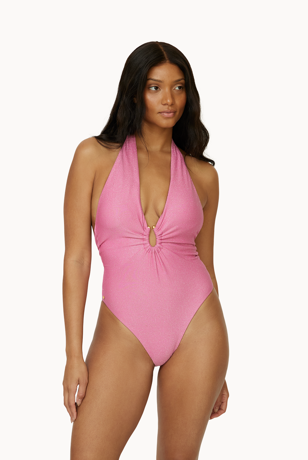 A woman wearing a pink one piece swimsuit standing against a white wall.