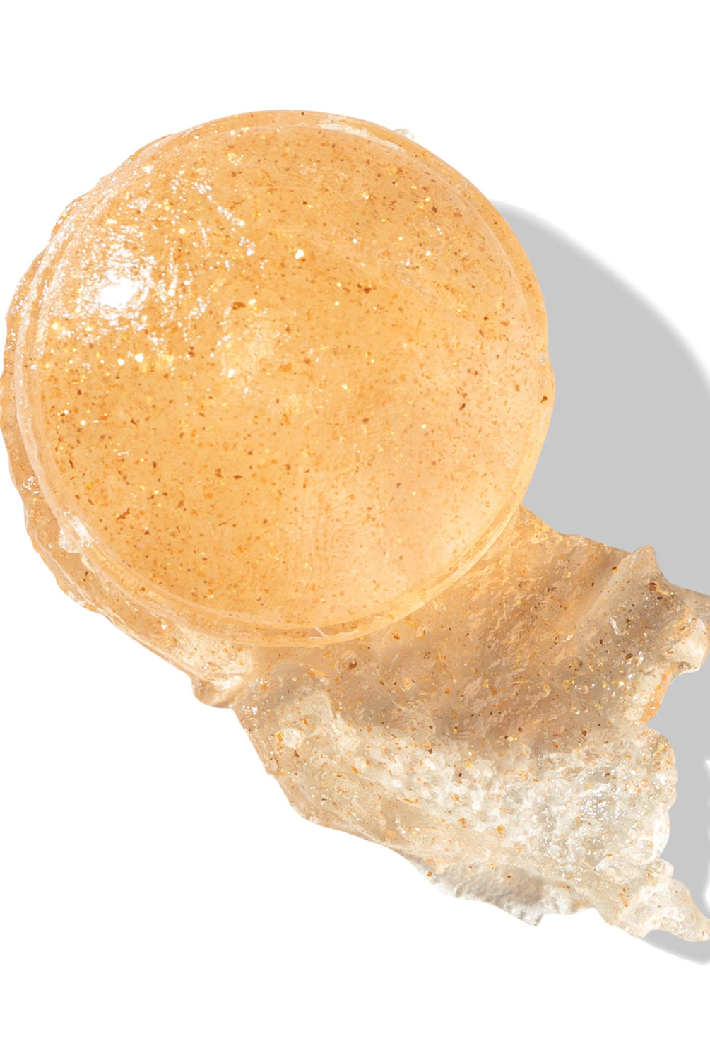 A close-up of the sheer stick product with a shimmery swatch smeared beside it.