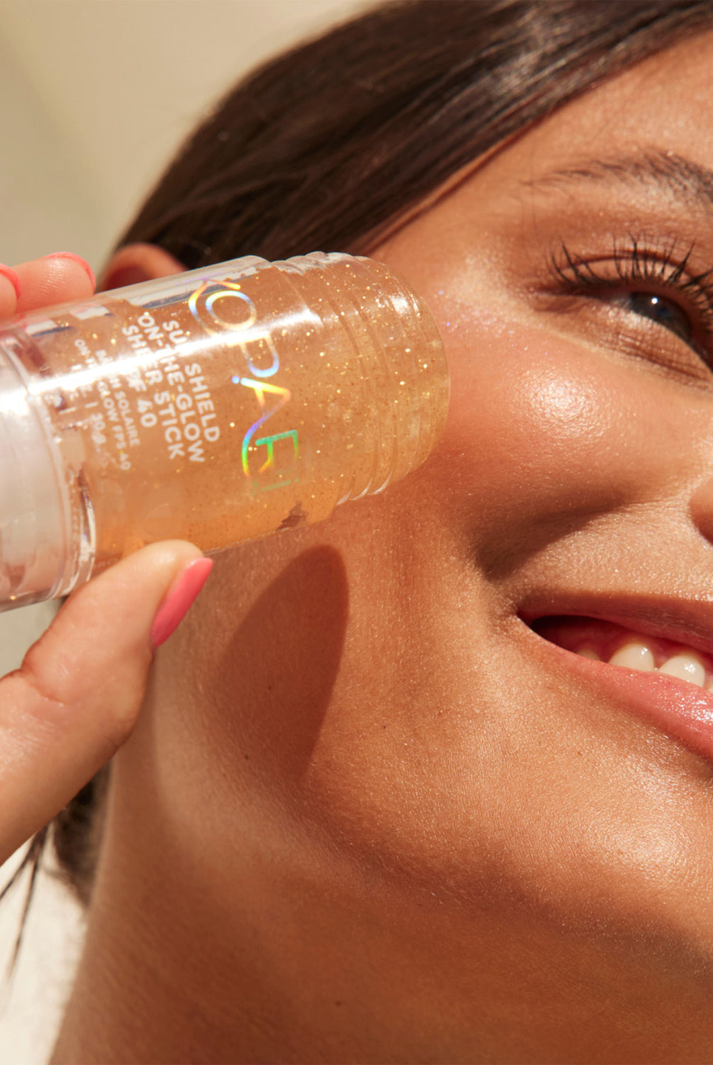 A smiling woman applying the Kopari Sun Shield stick to her cheek in direct sunlight.