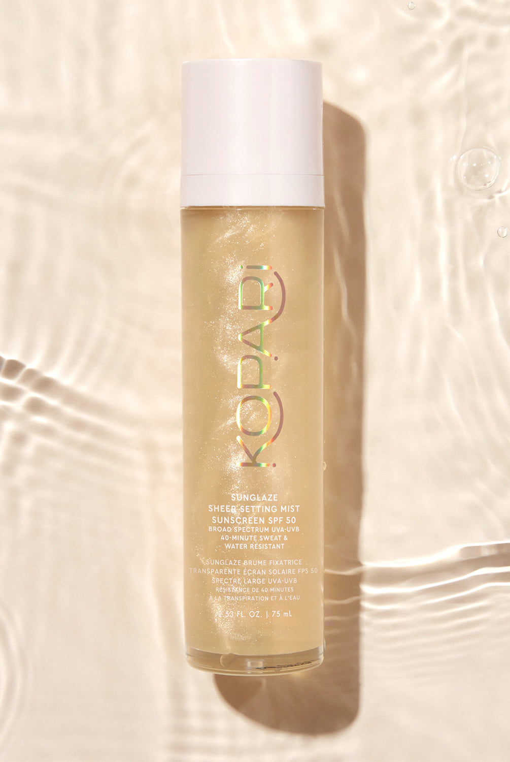 The Kopari Sun Shield spray bottle floating in water with ripples and sunlight reflecting off the surface.