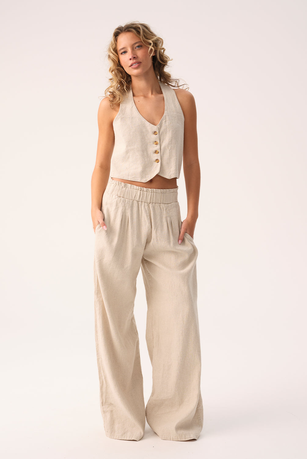 Woman wearing a beige sleeveless top and wide-leg pants on a white background