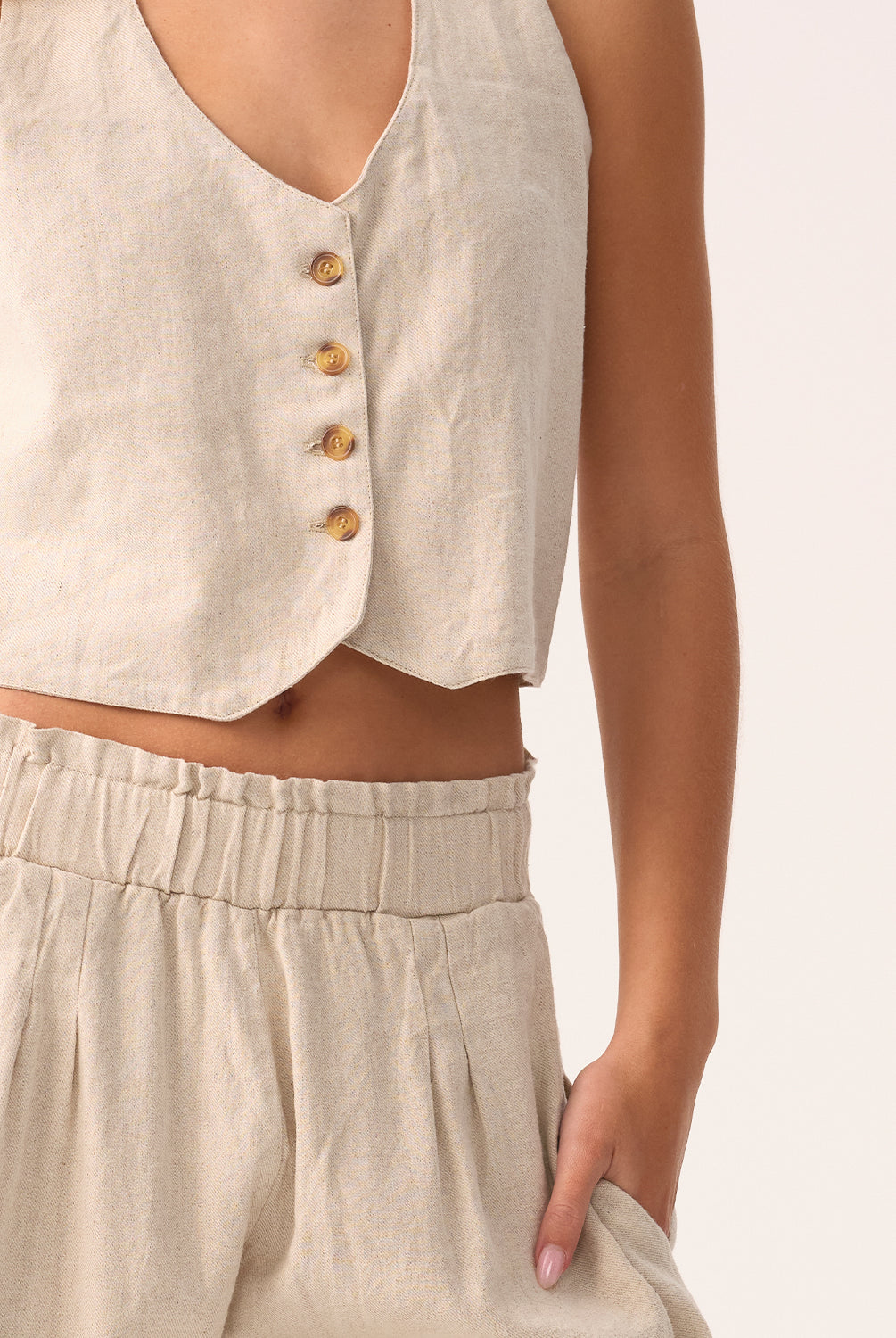 Beige sleeveless top with button details and matching pants on a neutral background
