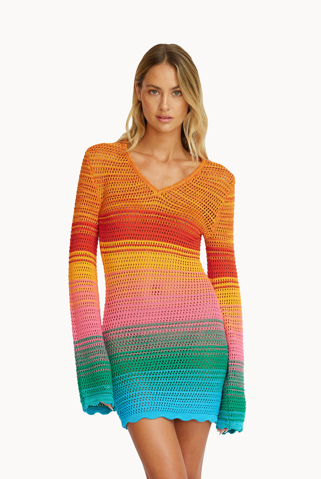 A woman wearing a multi-colored, knit, long sleeve dress standing in front of a white wall.