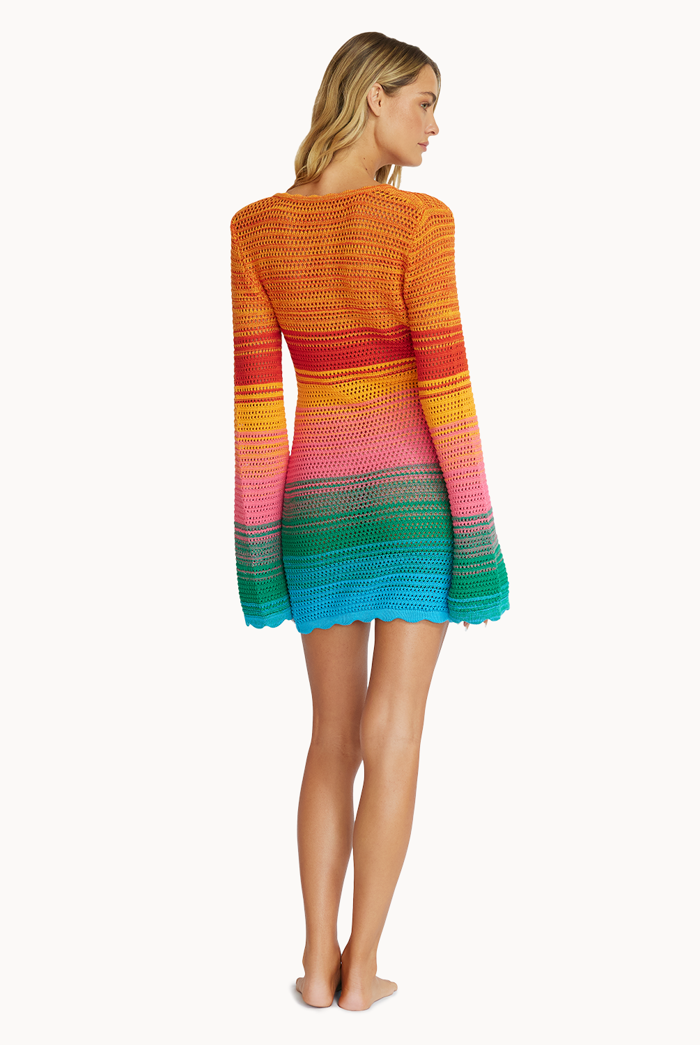A woman wearing a multi-colored, knit, long sleeve dress facing towards a white wall.