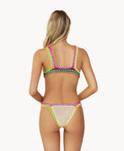 A blonde woman wearing a tan bikini facing towards a white wall.