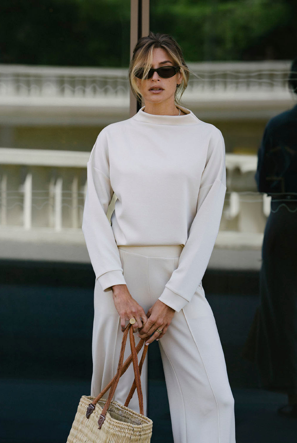 Woman in a beige outfit holding a straw bag outdoors