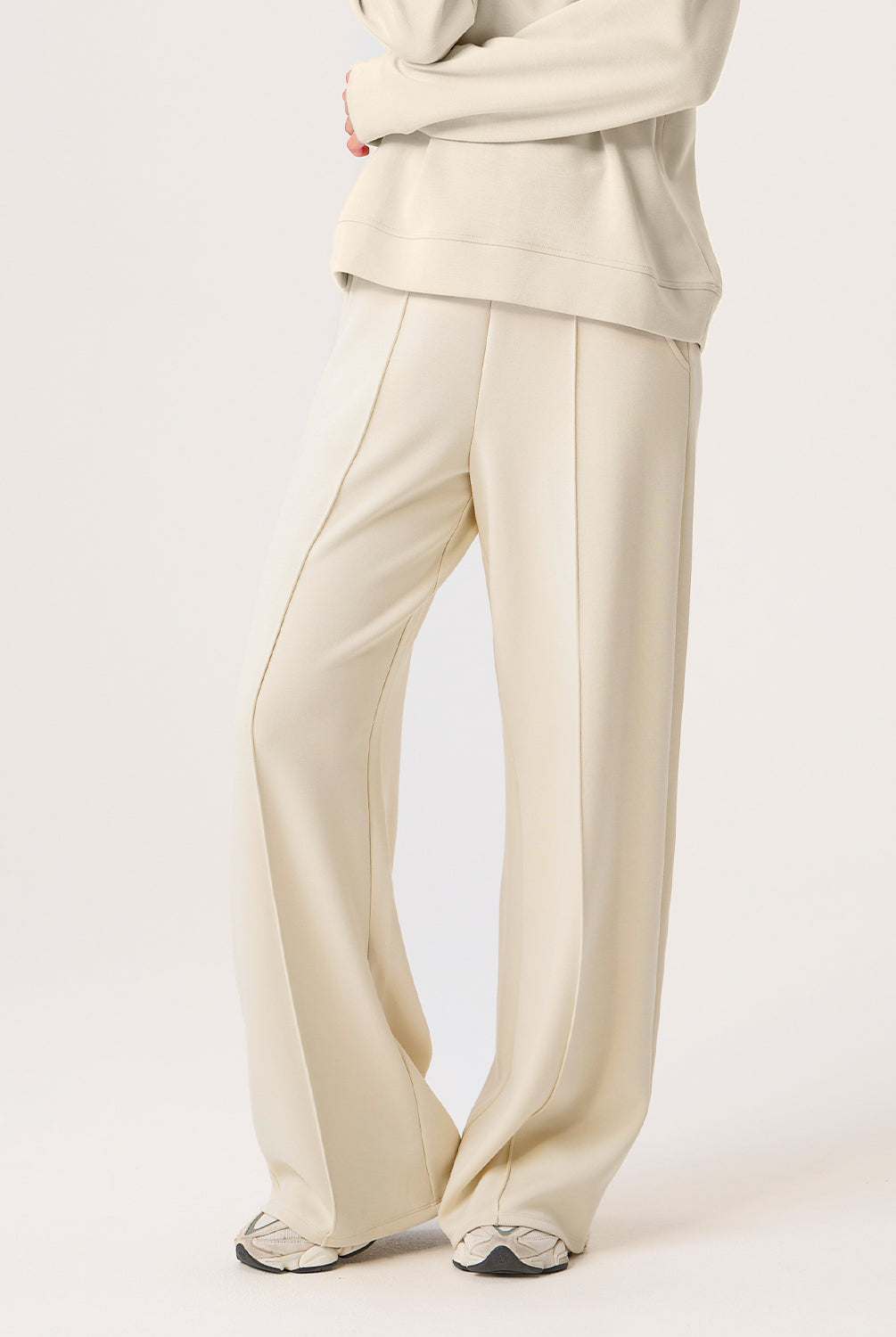 Woman wearing beige pants and top on a white background