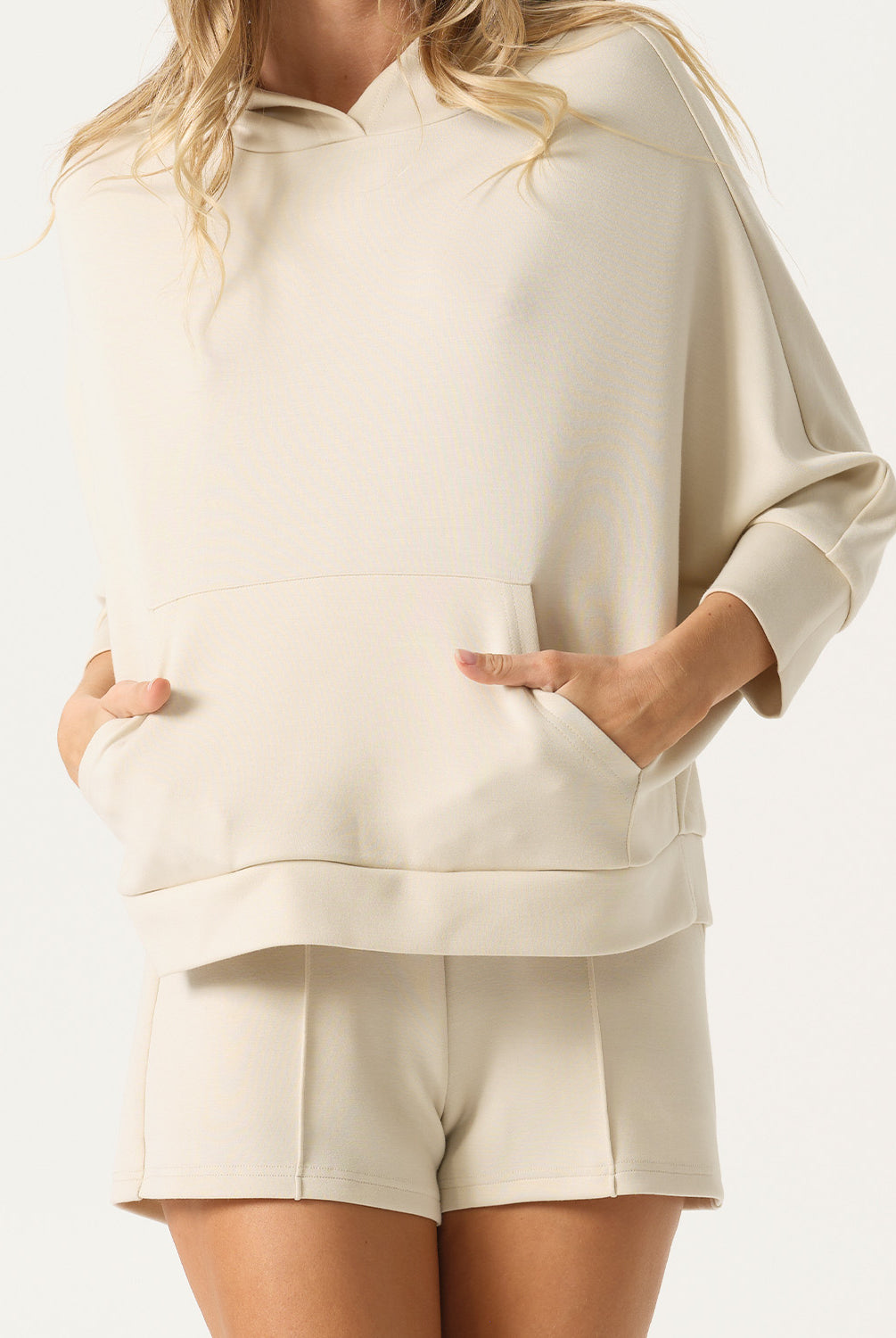 Person wearing a beige hoodie and shorts set on a white background
