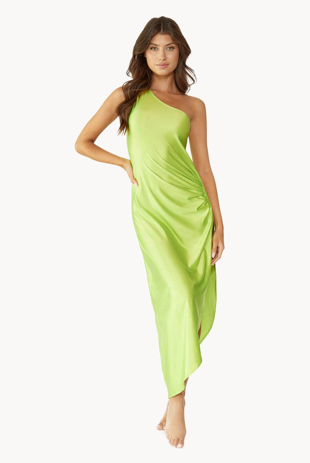 Brunette woman wearing a lime green one-shoulder dress with side slit and ring detail stands in front of white wall.