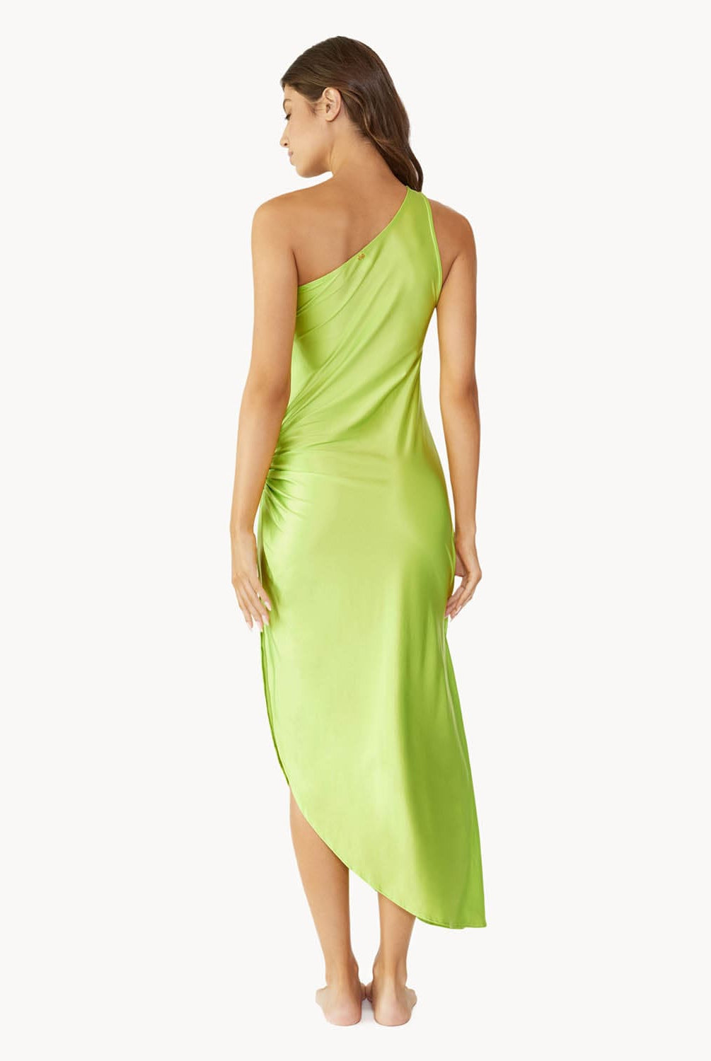 Brunette woman wearing a lime green one-shoulder dress with side slit and ring detail facing backwards towards a white wall.