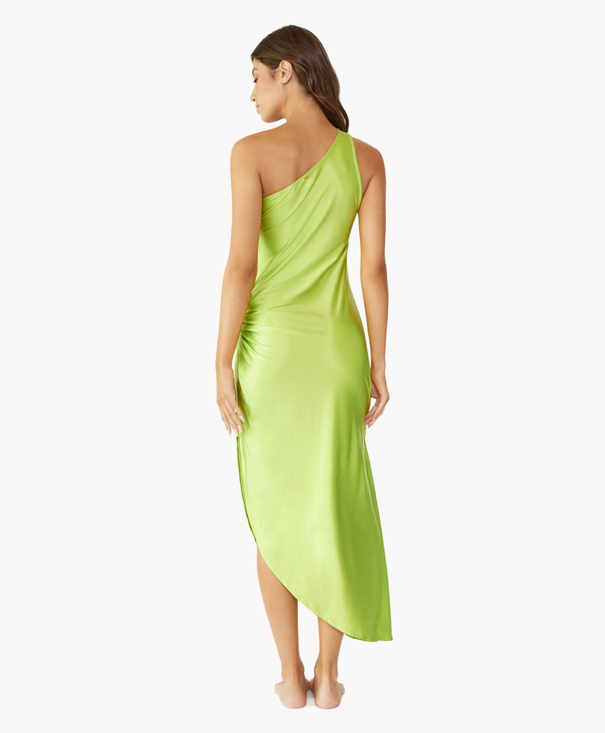 Brunette woman wearing a lime green one-shoulder dress with side slit and ring detail facing backwards towards a white wall.