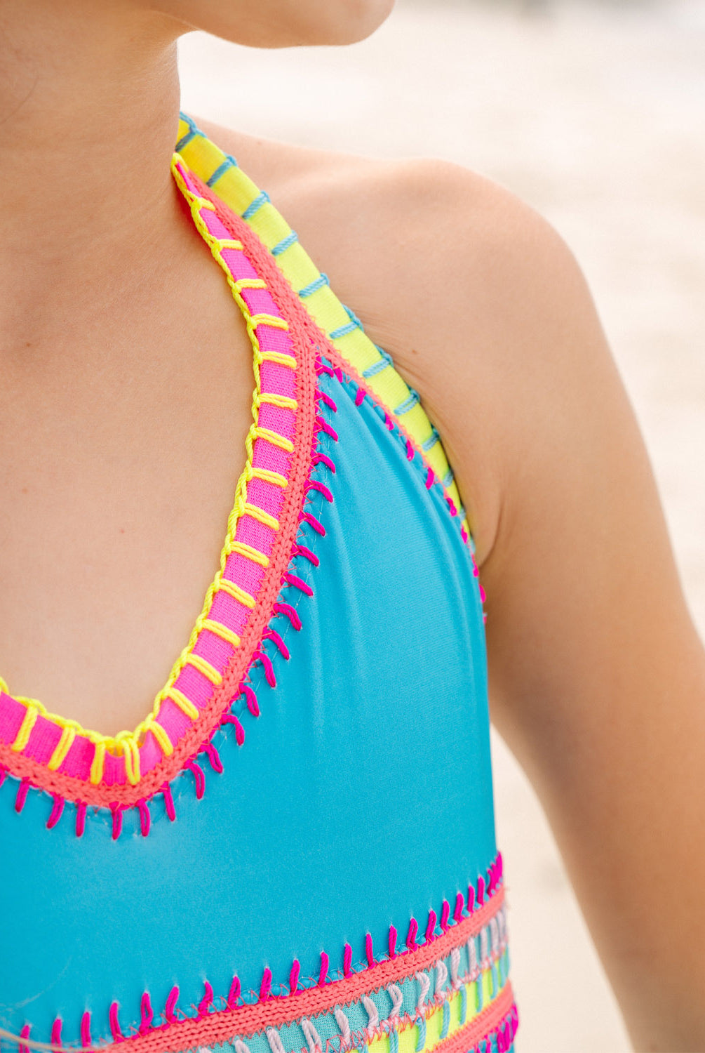 Close-up of a blue swimsuit with colorful trim on a blurred beach background