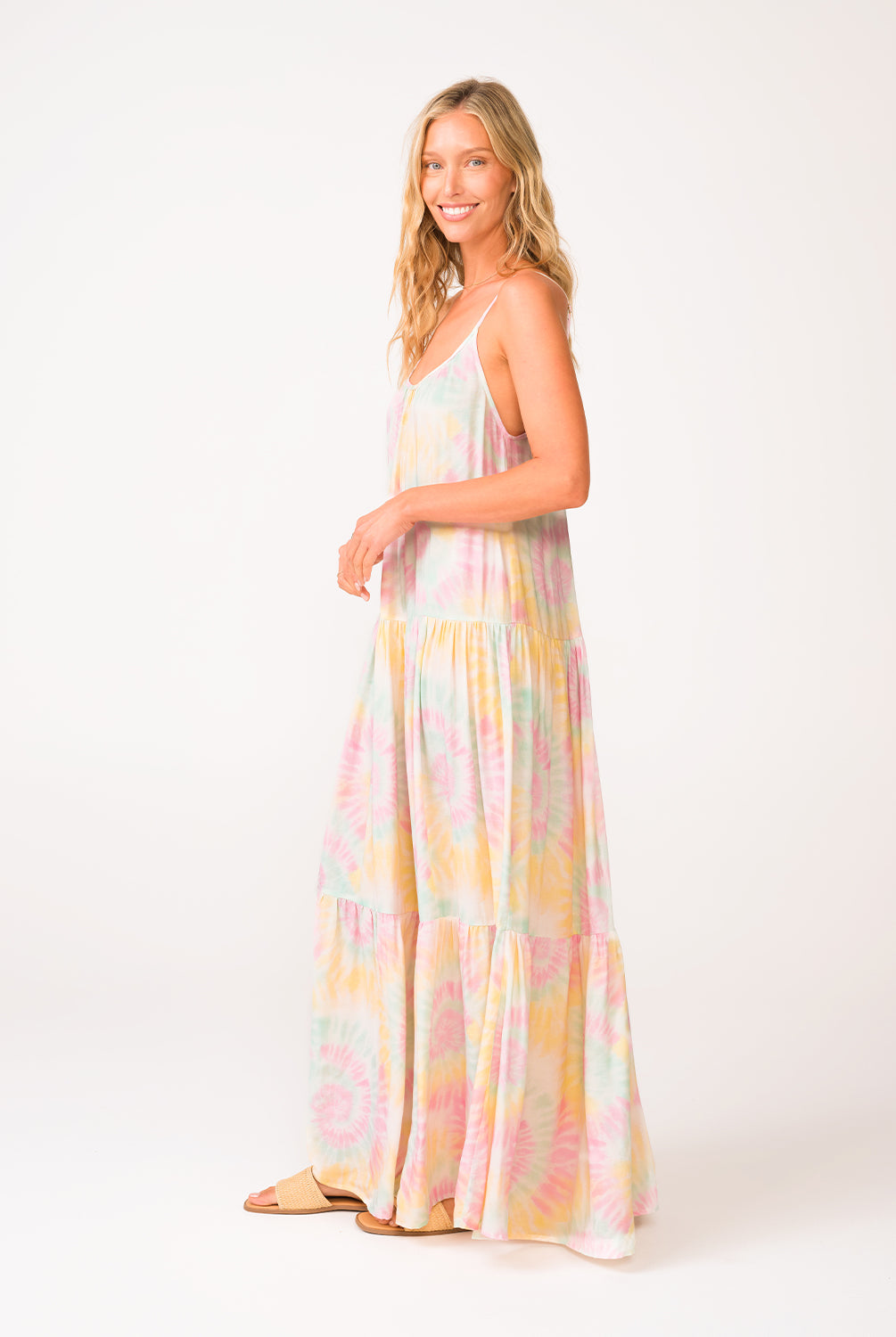 A woman wearing a tie dye long dress standing in front of a white wall.