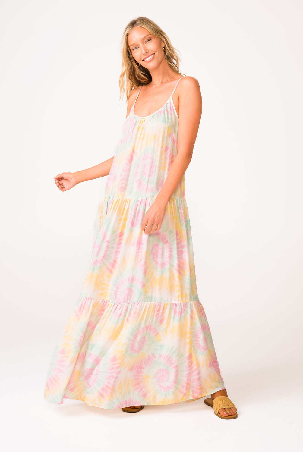 A woman wearing a tie dye long dress standing in front of a white wall.