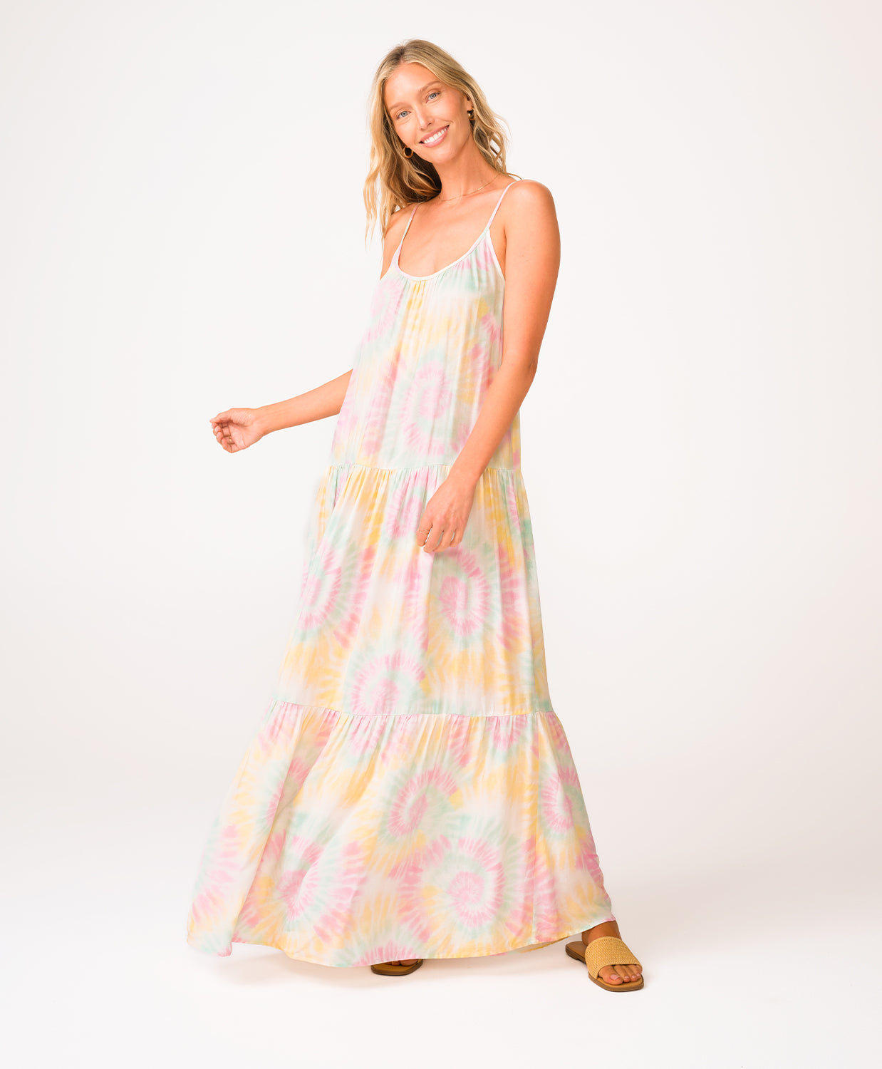 A woman wearing a tie dye long dress standing in front of a white wall.
