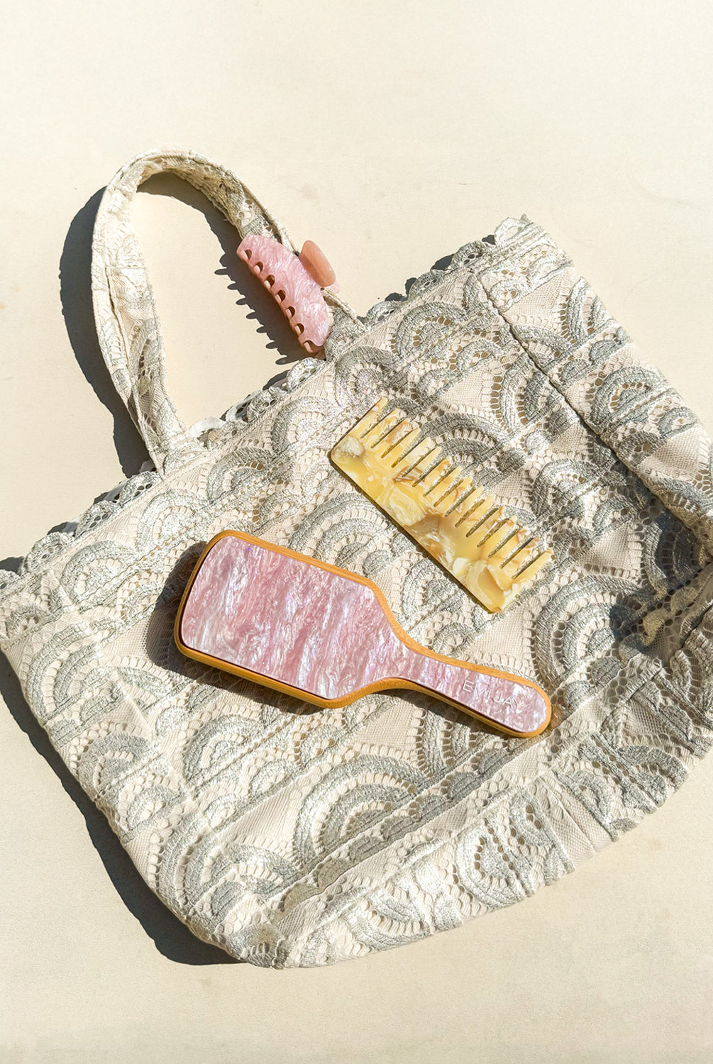 A tan lace tote with a brush, comb, and clip laying on white ground.