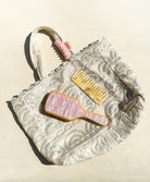 A tan lace tote with a brush, comb, and clip laying on white ground.