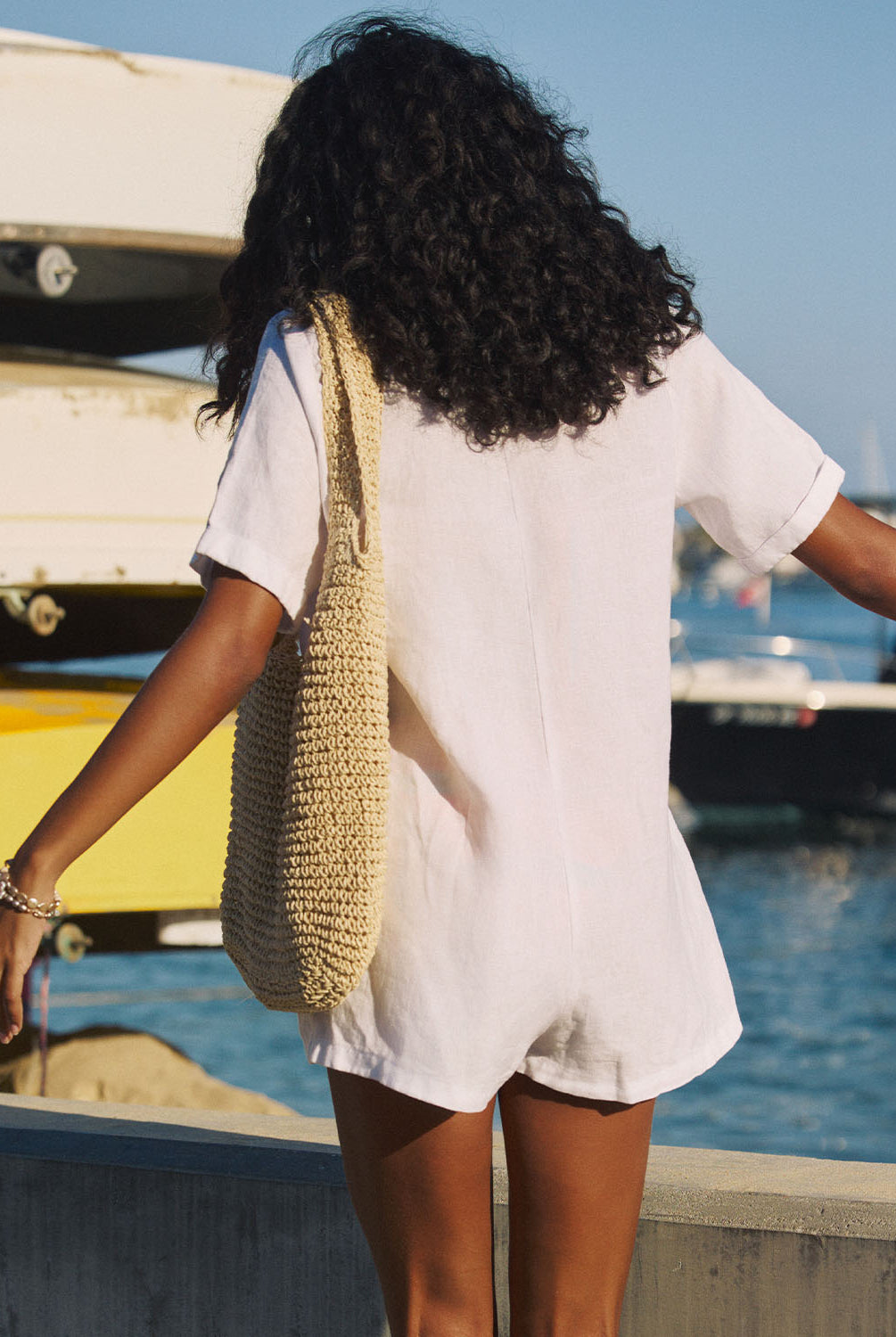 Woman with a woven bag walking by boats on a dock