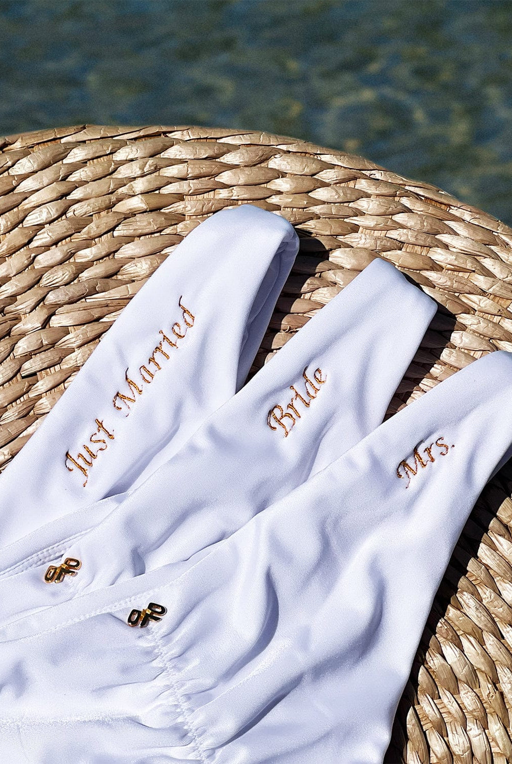 Three white bikini bottoms with gold embroidering laying flat on a wicker basket near the water.