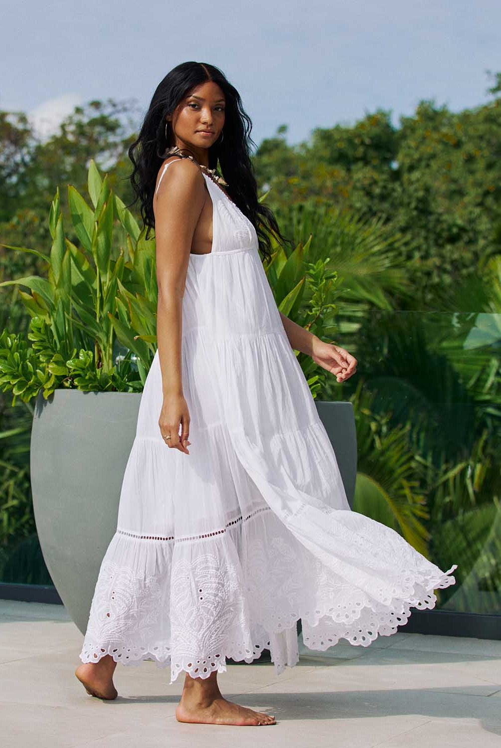 A woman wearing a long white dress standing outside near plants.
