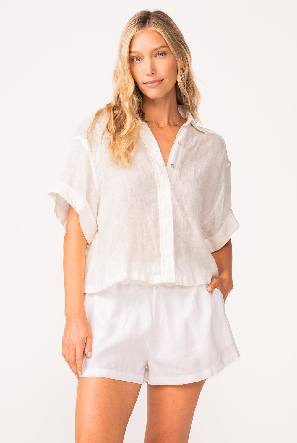 A woman wearing a matching white linen shirt and short set standing against a white wall.