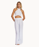 A woman wearing a white linen top and long linen pants standing in front of a white wall.