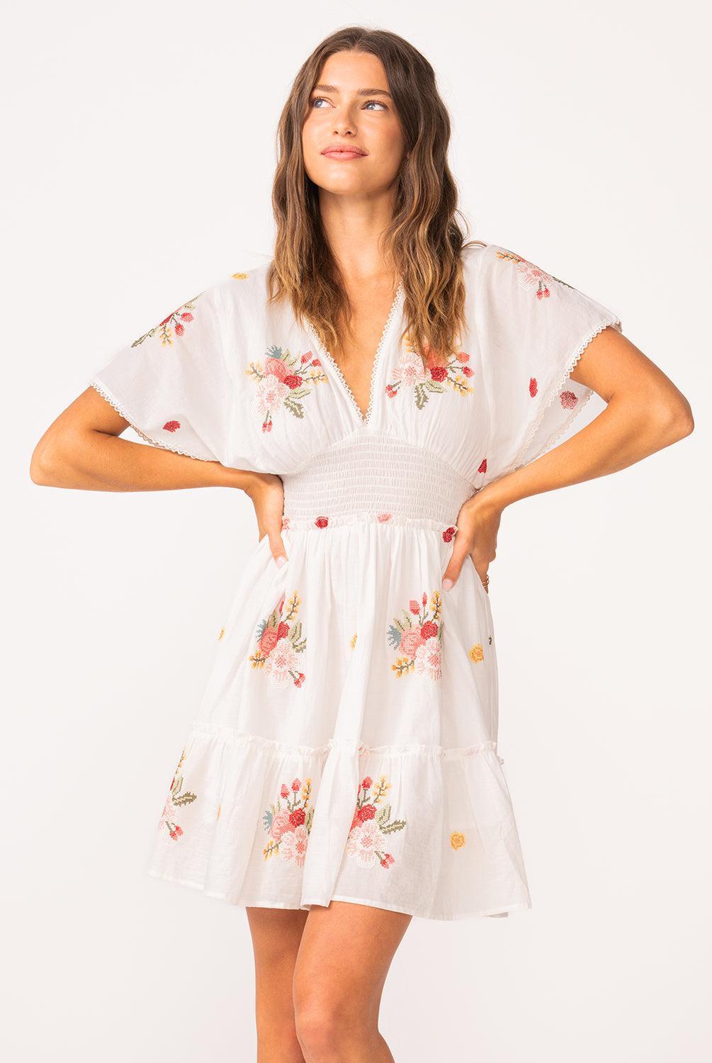 A woman wearing a short sleeve dress with floral details standing against a white wall.