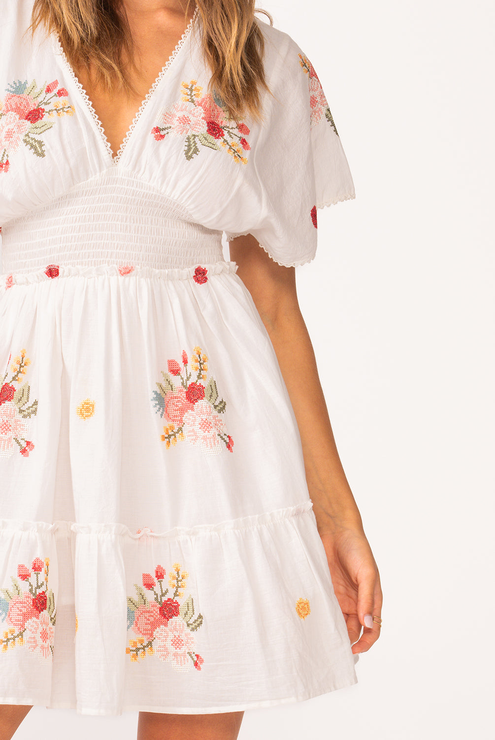 A woman wearing a short sleeve dress with floral details standing against a white wall.