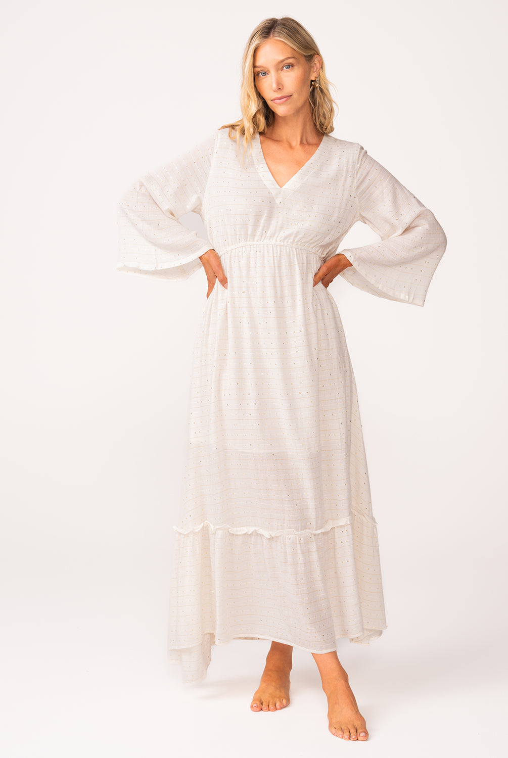 A woman wearing a long sleeve white dress standing against a white wall.