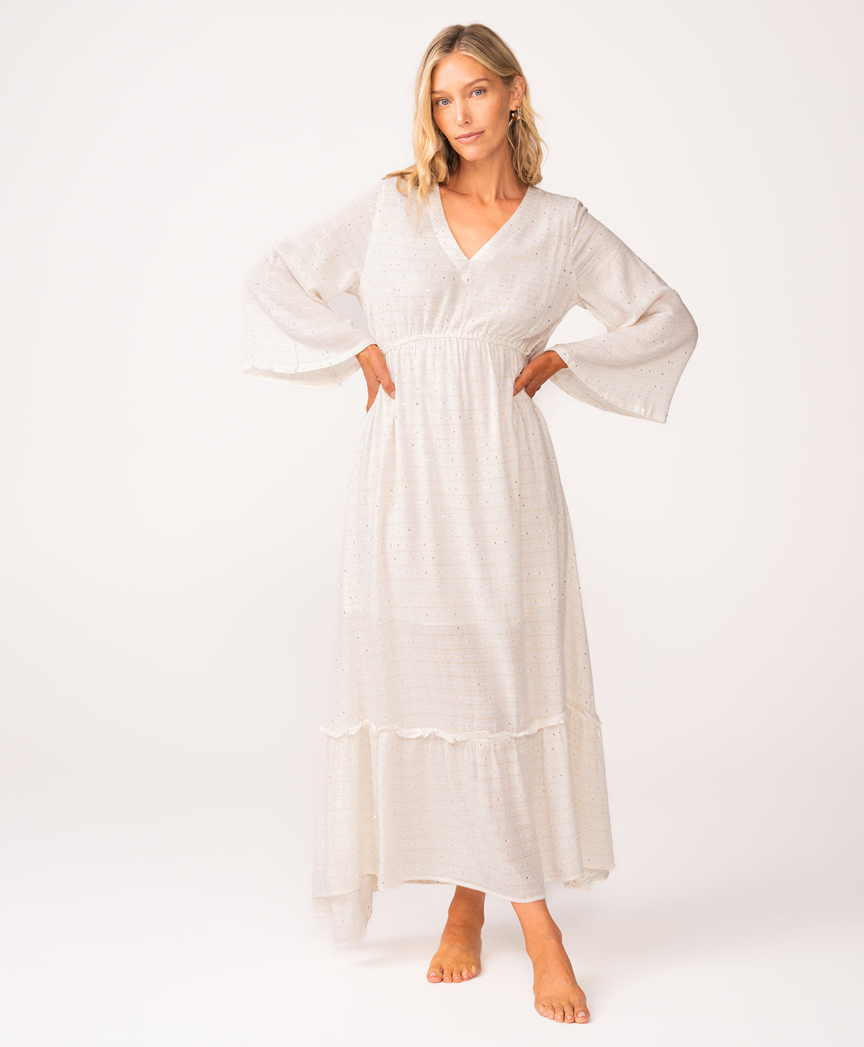 A woman wearing a long sleeve white dress standing against a white wall.