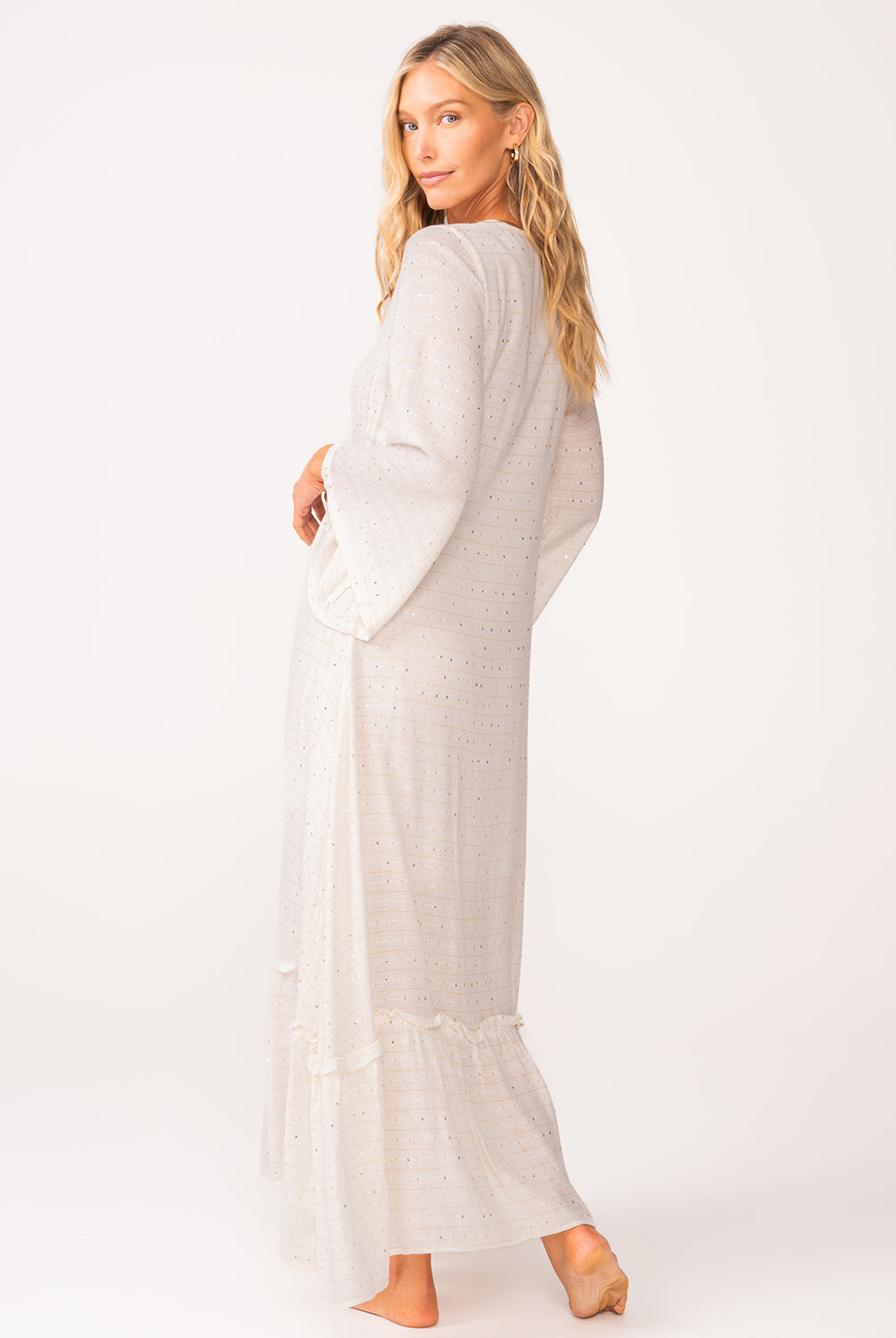 A woman wearing a long sleeve white dress standing against a white wall.