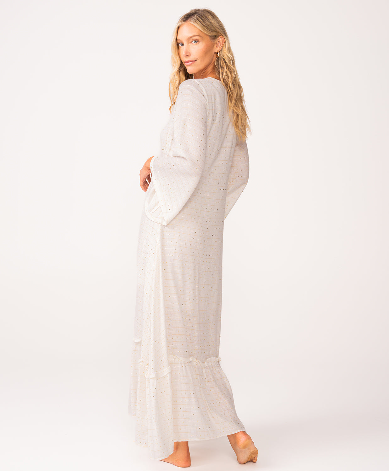 A woman wearing a long sleeve white dress standing against a white wall.