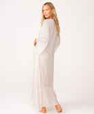 A woman wearing a long sleeve white dress standing against a white wall.