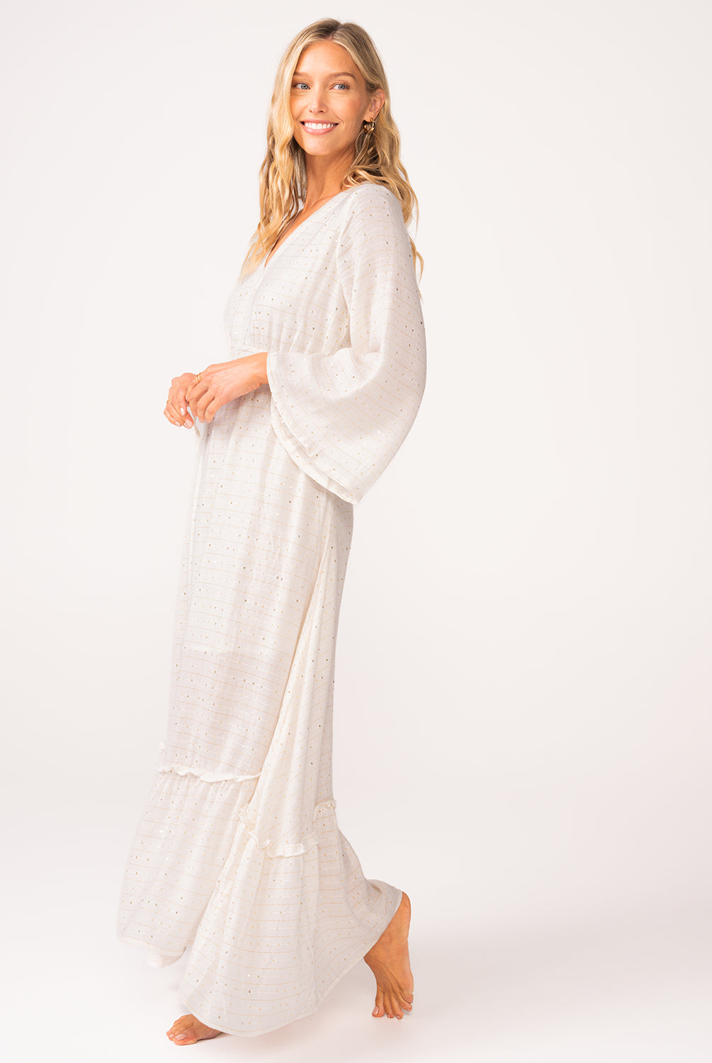 A woman wearing a long sleeve white dress standing against a white wall.