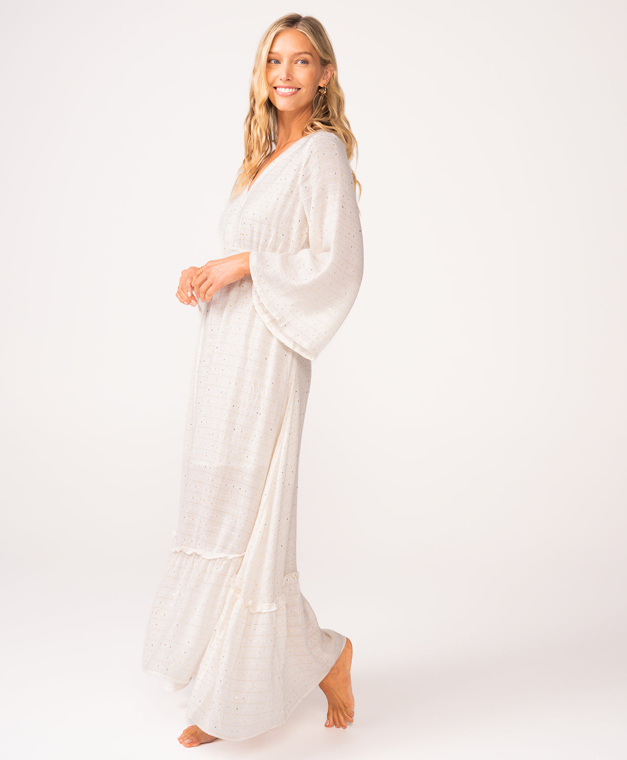 A woman wearing a long sleeve white dress standing against a white wall.
